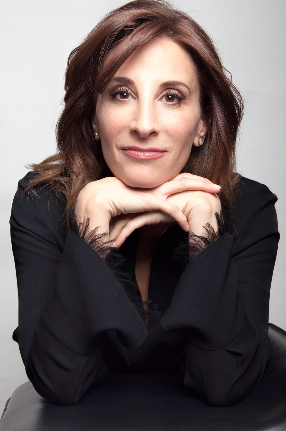 Headshot of an actor resting her chin on her hands, in a black blouse