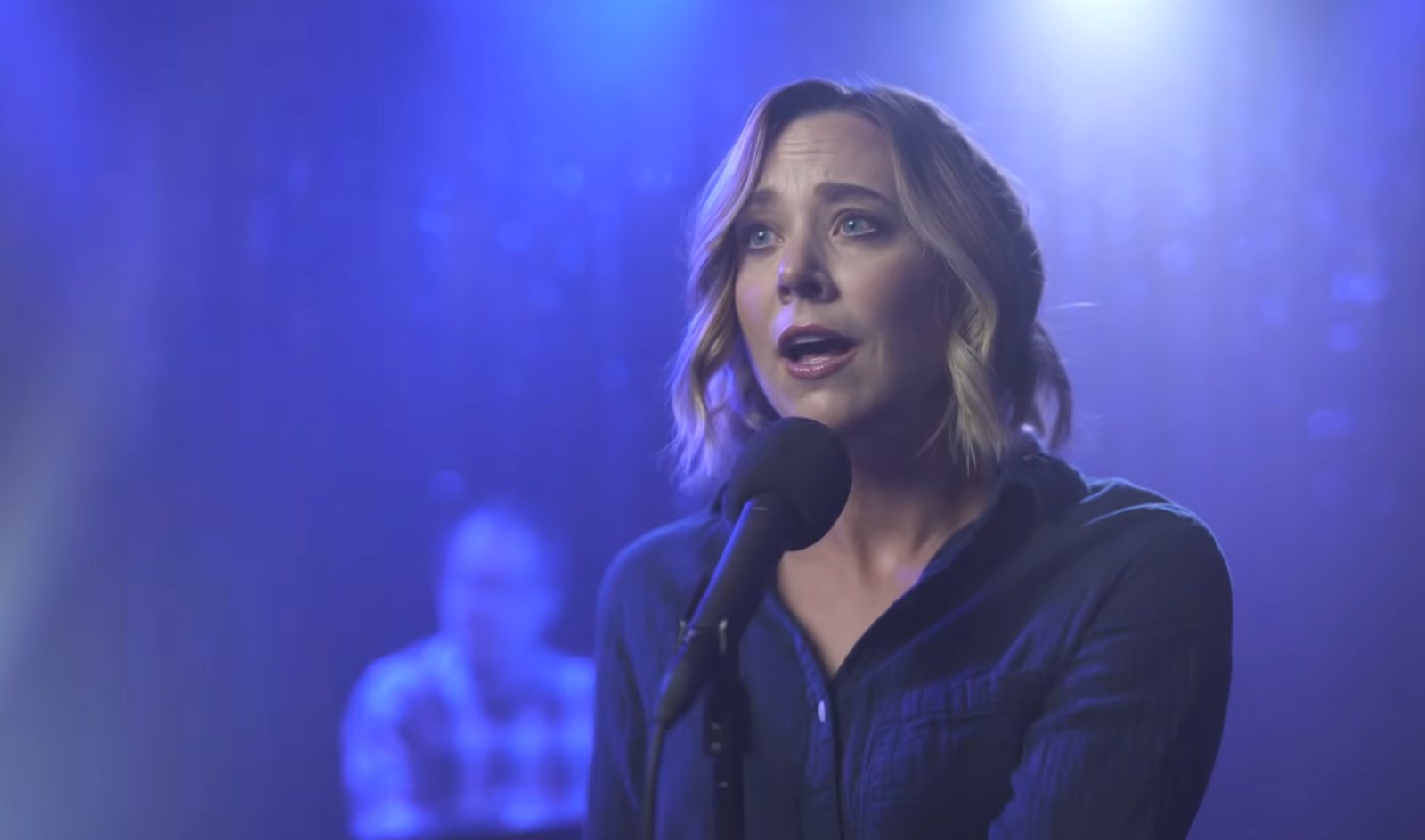 A singer performs at a microphone in blue light