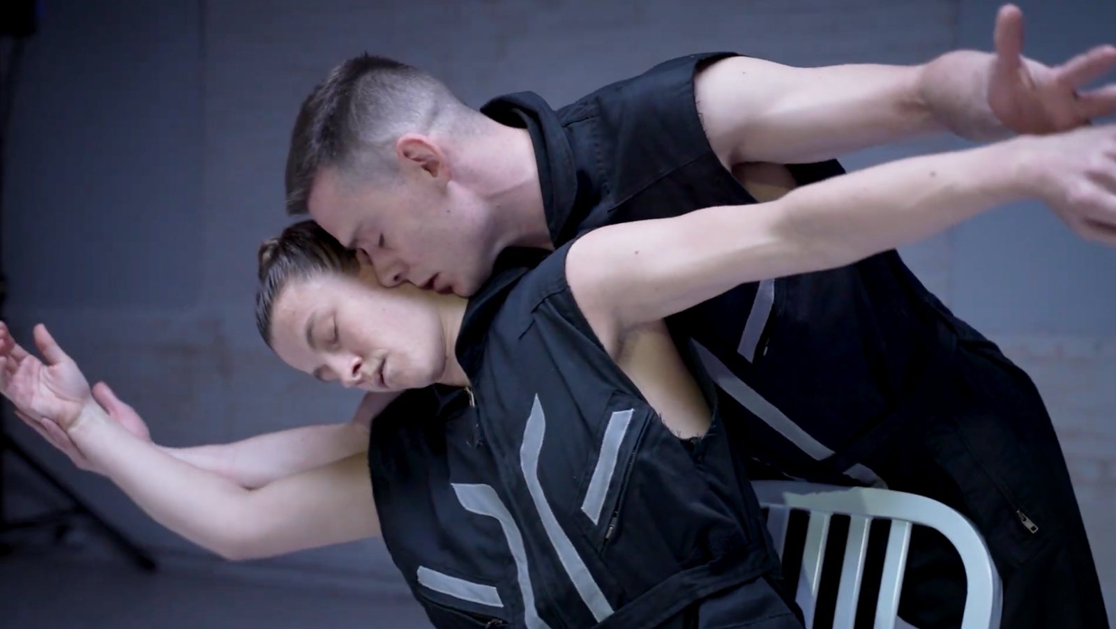 Two dancers in black vests lean into each other