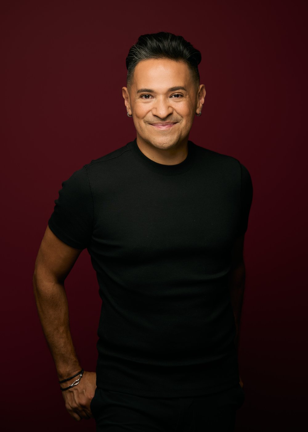 Roberto Araujo, smiling, in a black tee against a deep red backdrop